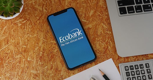 Ecobank Phone App with Stationery and Macbook. Ecobank is a pan-African banking conglomerate