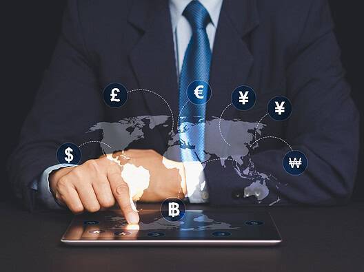 Businessman using tablet with global currency symbols and world map.