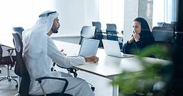 Man and woman with traditional clothes working in a business office of Dubai. Portraits of successful entrepreneurs businessman and businesswoman in formal emirates outfits. Concept about middle east