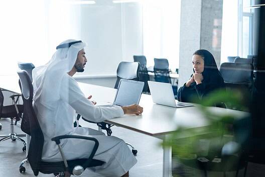 Man and woman with traditional clothes working in a business office of Dubai. Portraits of successful entrepreneurs businessman and businesswoman in formal emirates outfits. Concept about middle east
