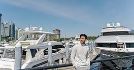 Portrait of asian rich man standing near expensive yachts, looking away outdoors. Attractive chinese male posing for picture, on street
