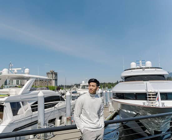 Portrait of asian rich man standing near expensive yachts, looking away outdoors. Attractive chinese male posing for picture, on street