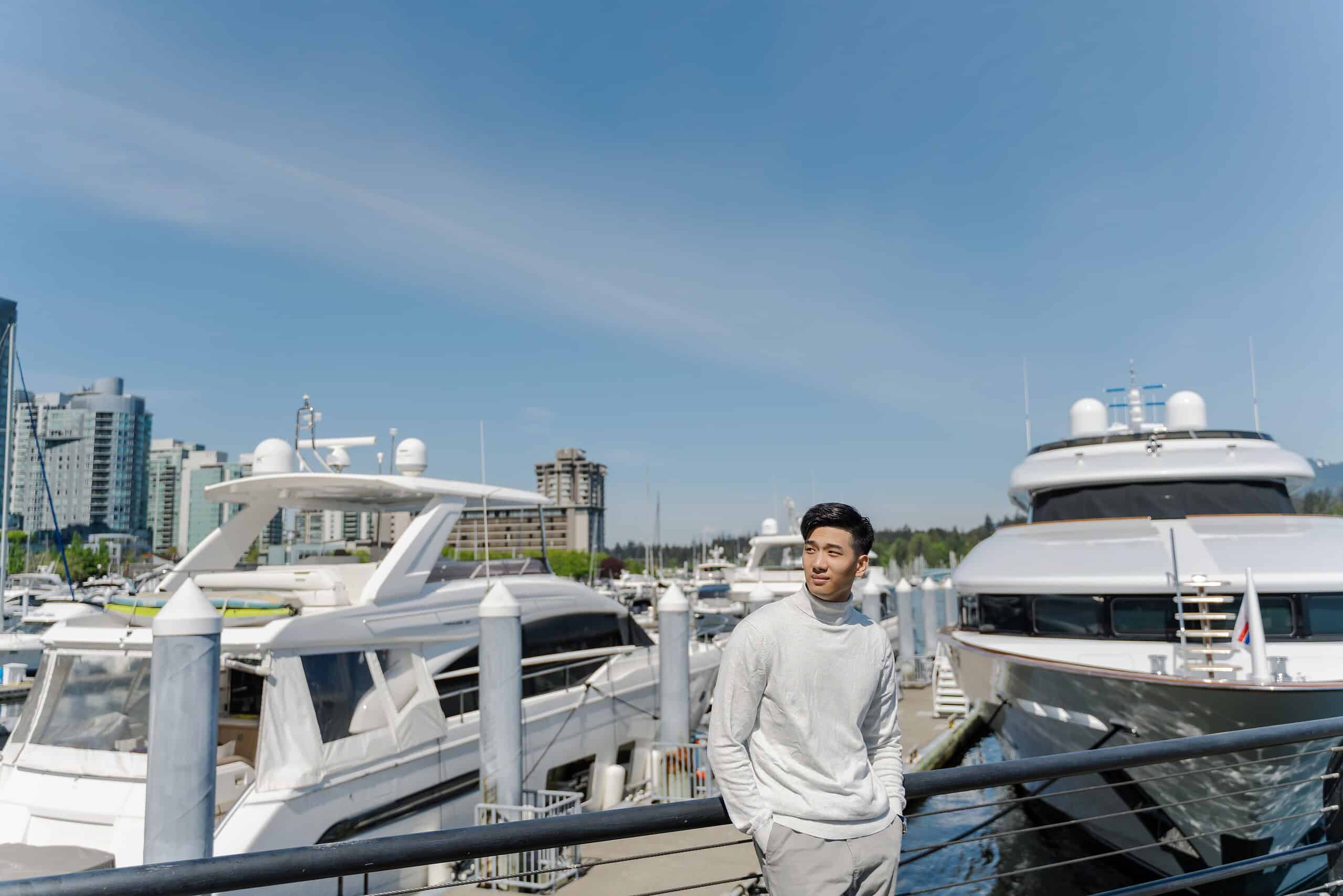 Portrait of asian rich man standing near expensive yachts, looking away outdoors. Attractive chinese male posing for picture, on street