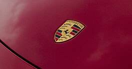 The Porsche logo on the hood of a red 718 Boxster GTS sports car.