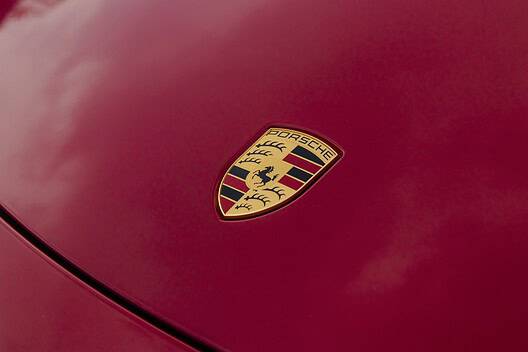 The Porsche logo on the hood of a red 718 Boxster GTS sports car.
