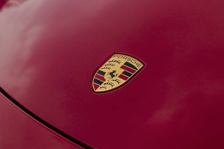 The Porsche logo on the hood of a red 718 Boxster GTS sports car.