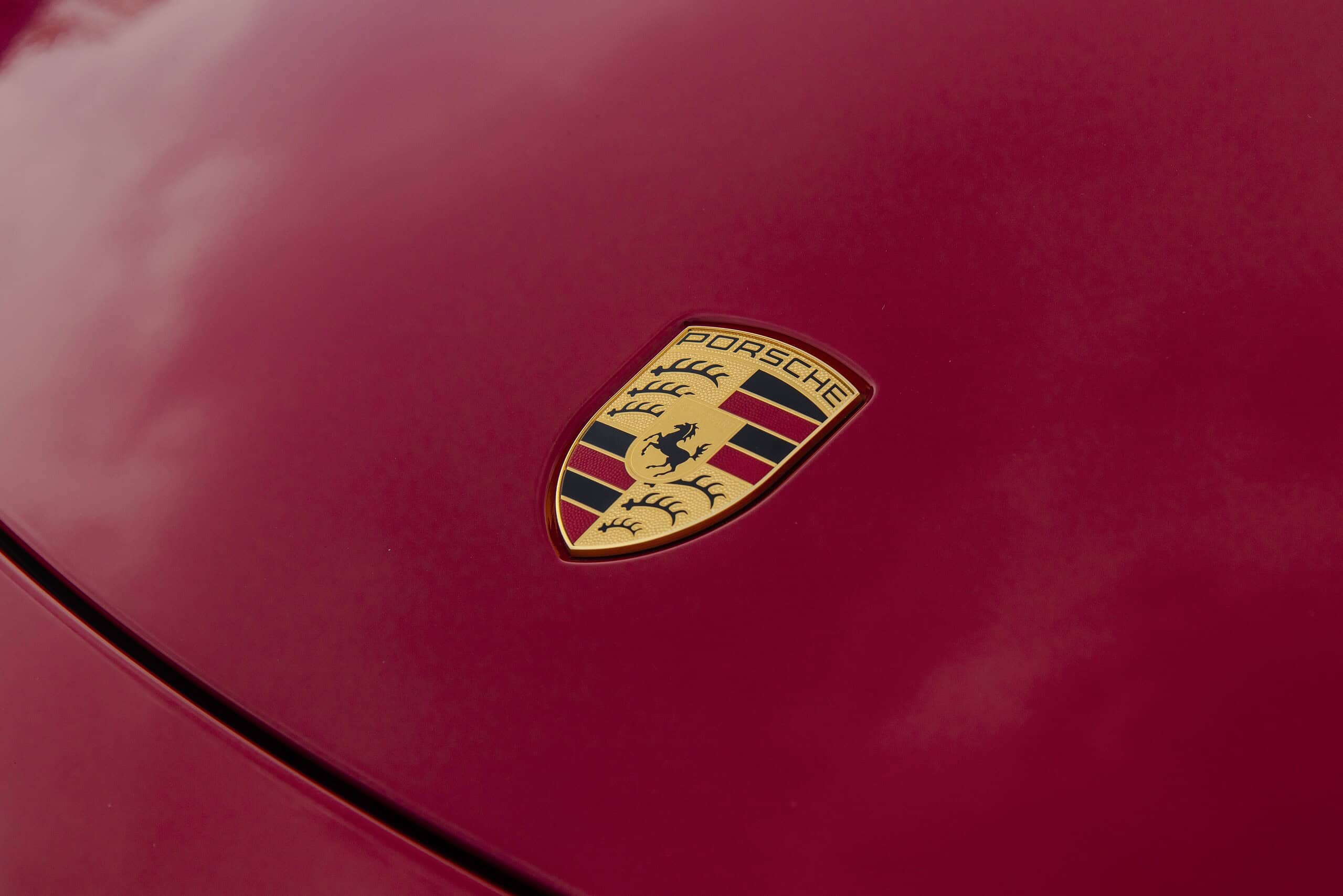 The Porsche logo on the hood of a red 718 Boxster GTS sports car.
