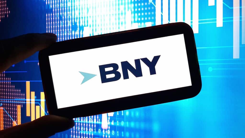 BNY logo is seen in a cell phone with a chart in the background.