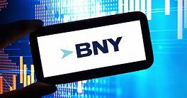 BNY logo is seen in a cell phone with a chart in the background.