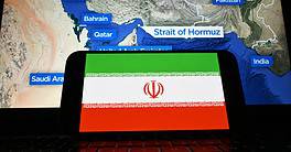 The Iranian flag is visible on the screen. After U.S. attacks, Iran decided to close the Strait of Hormuz.
