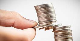 Closeup fingers try to pull out some money coins from the heap and risk to take the whole coins falling down, balance, planning and risk in business and finance concept