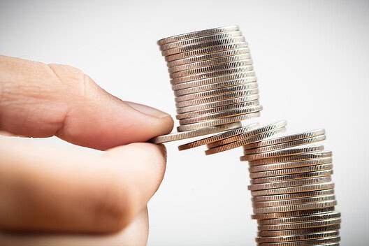 Closeup fingers try to pull out some money coins from the heap and risk to take the whole coins falling down, balance, planning and risk in business and finance concept