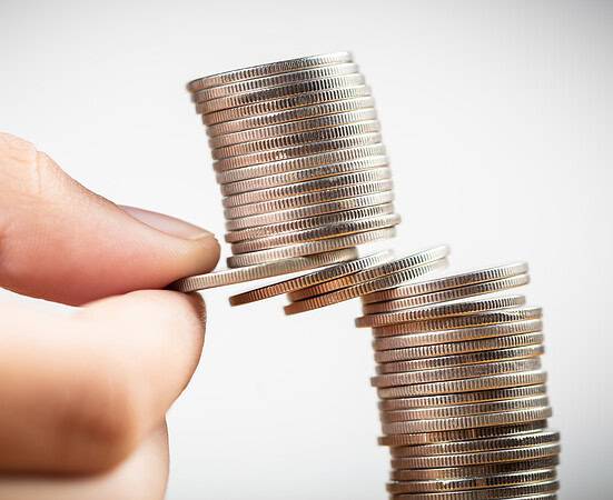 Closeup fingers try to pull out some money coins from the heap and risk to take the whole coins falling down, balance, planning and risk in business and finance concept