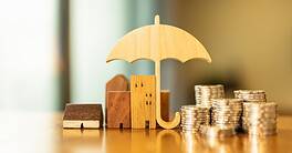 Model of umbrella with house and coins on wooden table concept of the system of insurance savings and the cost of health insurance.