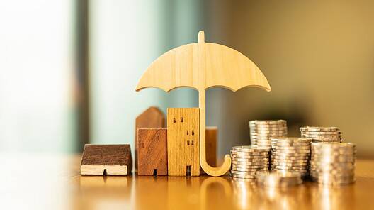 Model of umbrella with house and coins on wooden table concept of the system of insurance savings and the cost of health insurance.