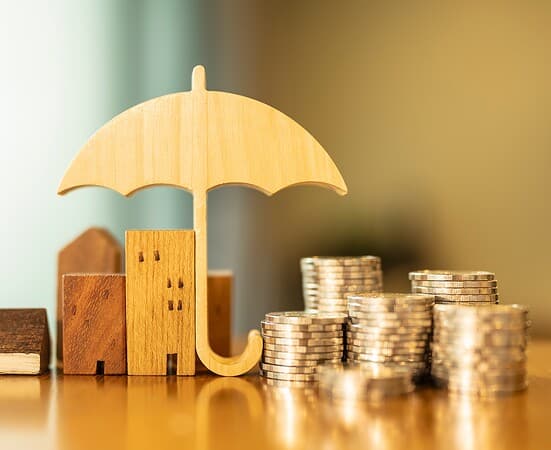 Model of umbrella with house and coins on wooden table concept of the system of insurance savings and the cost of health insurance.
