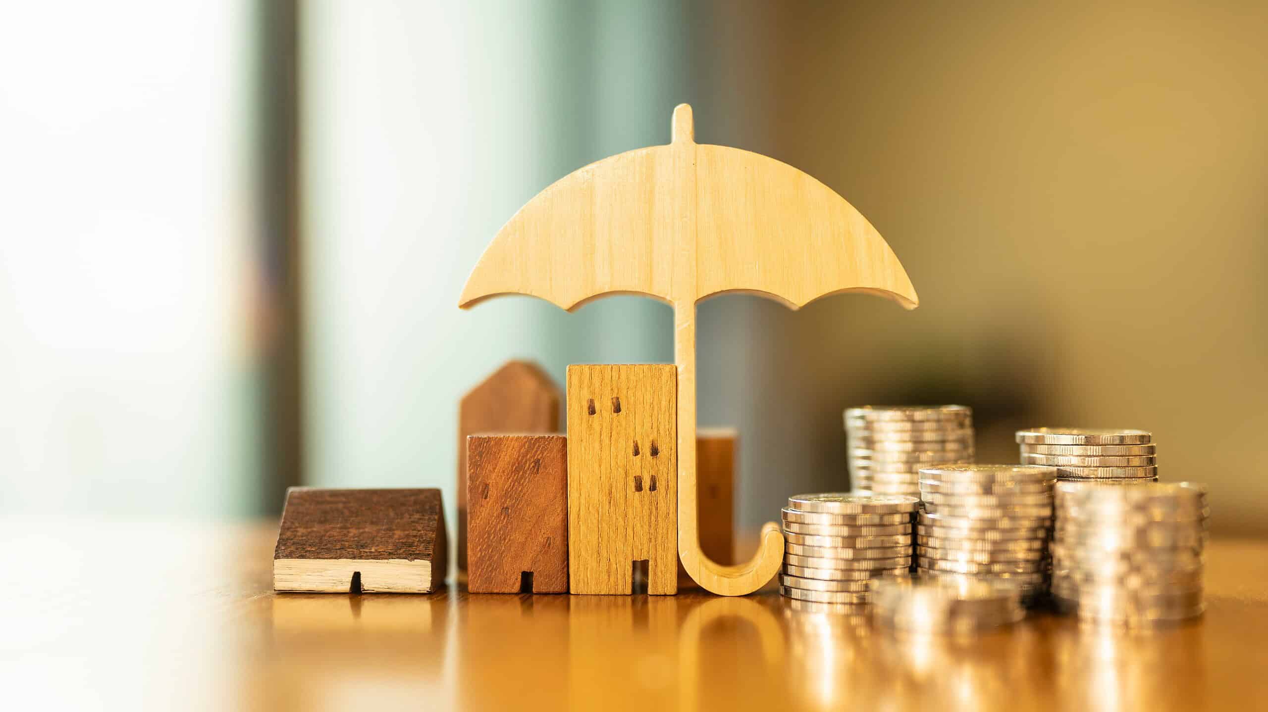 Model of umbrella with house and coins on wooden table concept of the system of insurance savings and the cost of health insurance.