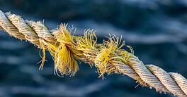 Frayed rope near to break on blue sea water background. Selective focus.