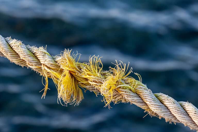Frayed rope near to break on blue sea water background. Selective focus.