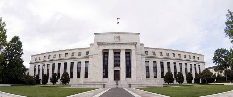 Federal Reserve building with a flag on top and surrounding trees.