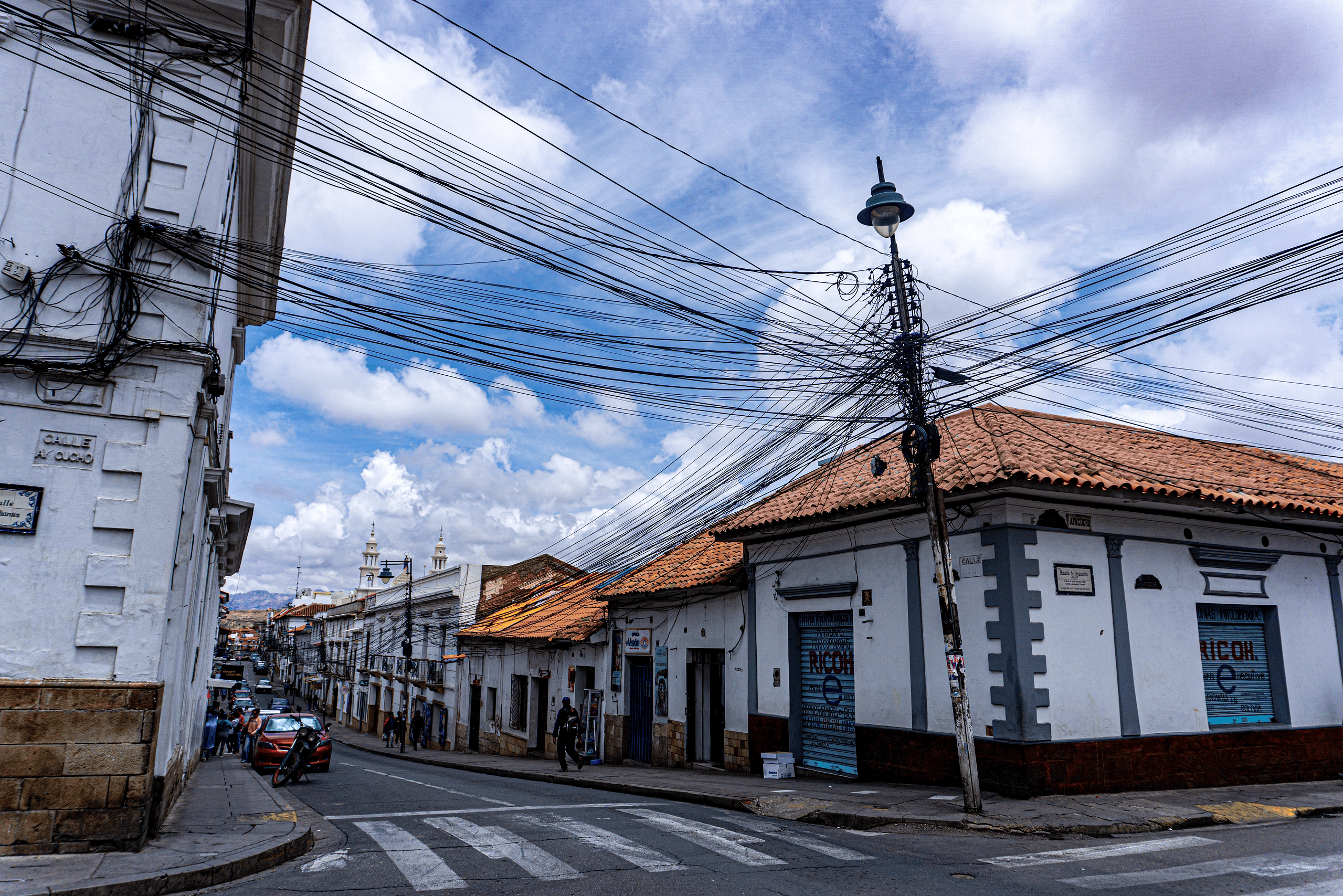 Typical street with white walls colonial architecture and a web of electrical wires creating contrast between the past and present in the city in Sucre, Bolivia