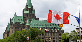 Ottawa Parliament Hill with Canadian flags and historic architecture.