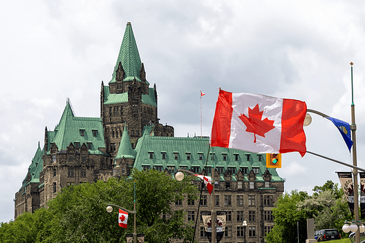Ottawa Parliament Hill with Canadian flags and historic architecture.