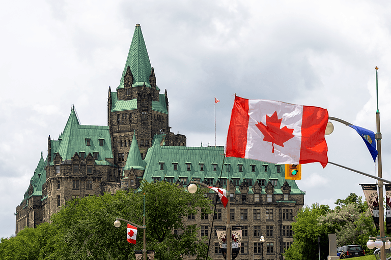 Ottawa Parliament Hill with Canadian flags and historic architecture.