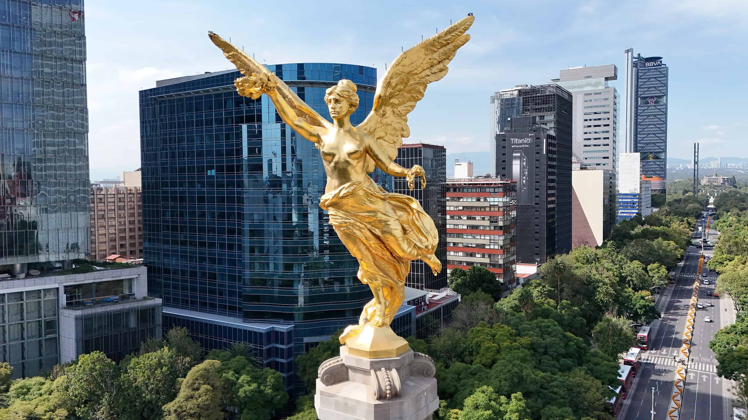 Golden angel statue overlooking Mexico City skyline and green parks.