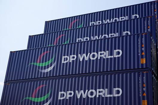 Global Logistics and Supply Chain Concept with Stacked dark blue containers for marine shipping of DP World logistics, with its logs DP WORLD clearly painted in white on the dark blue coating of the containers against blue sky in a container yard