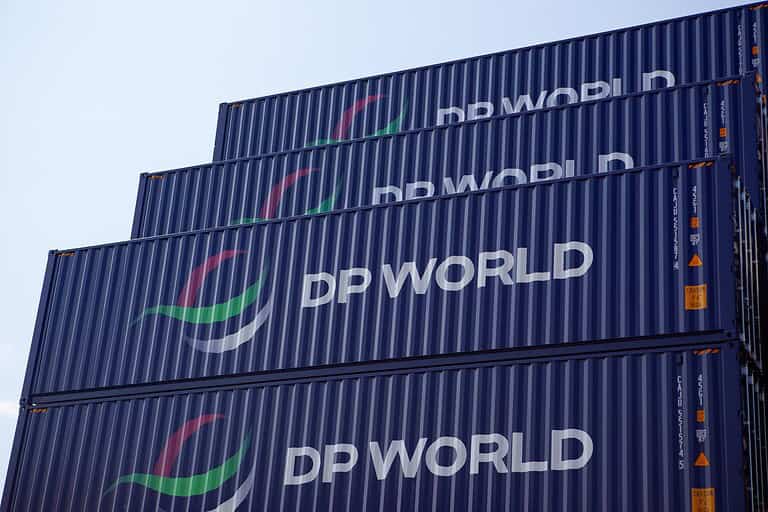 Global Logistics and Supply Chain Concept with Stacked dark blue containers for marine shipping of DP World logistics, with its logs DP WORLD clearly painted in white on the dark blue coating of the containers against blue sky in a container yard