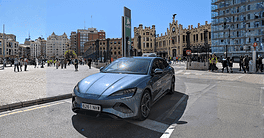 Blue BYD electric vehicle parked in urban city square with historic buildings.