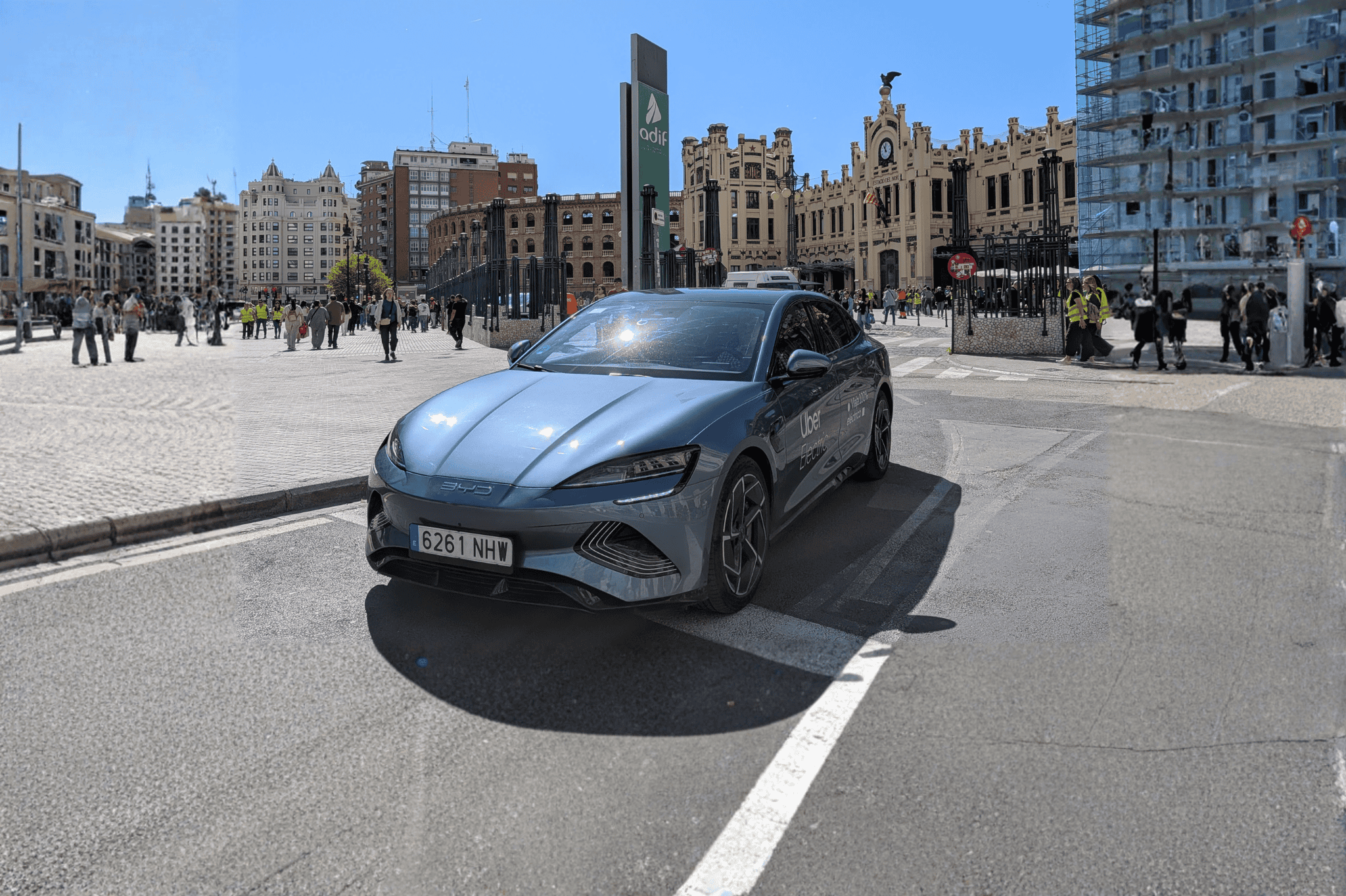 Blue BYD electric vehicle parked in urban city square with historic buildings.