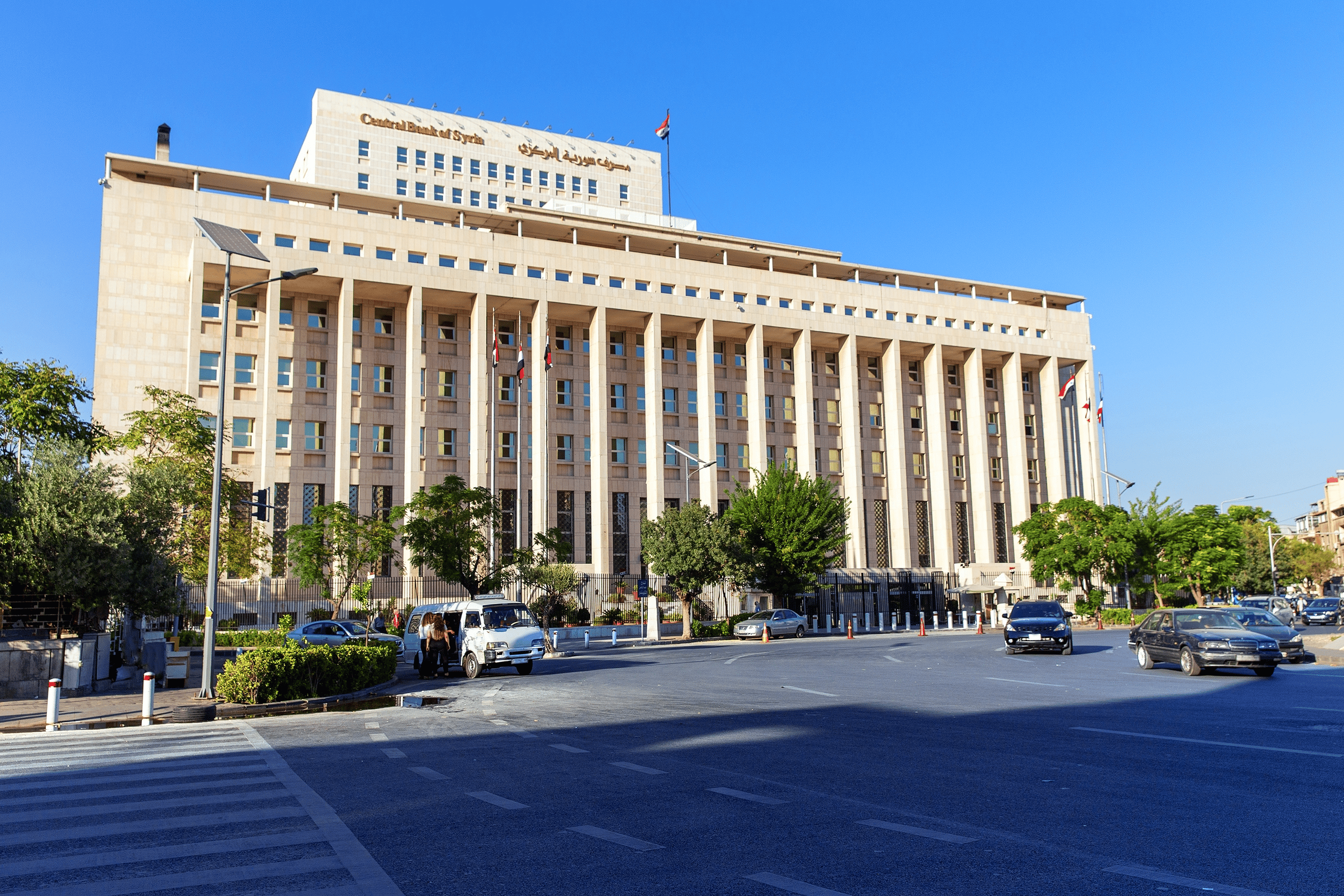 Central Bank building in Syria with flags and trees.