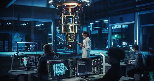 Female Engineer Working on Quantum Computer Hardware, Using Tablet Computer to Access Technical Specifications and Control Processor Parameters. Group of Developers Work on AI Behind a Desk
