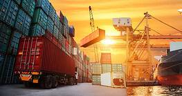 Cargo ship, containers, cranes, and airplane at sunset.