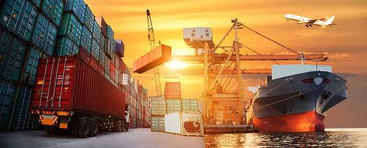 Cargo ship, containers, cranes, and airplane at sunset.