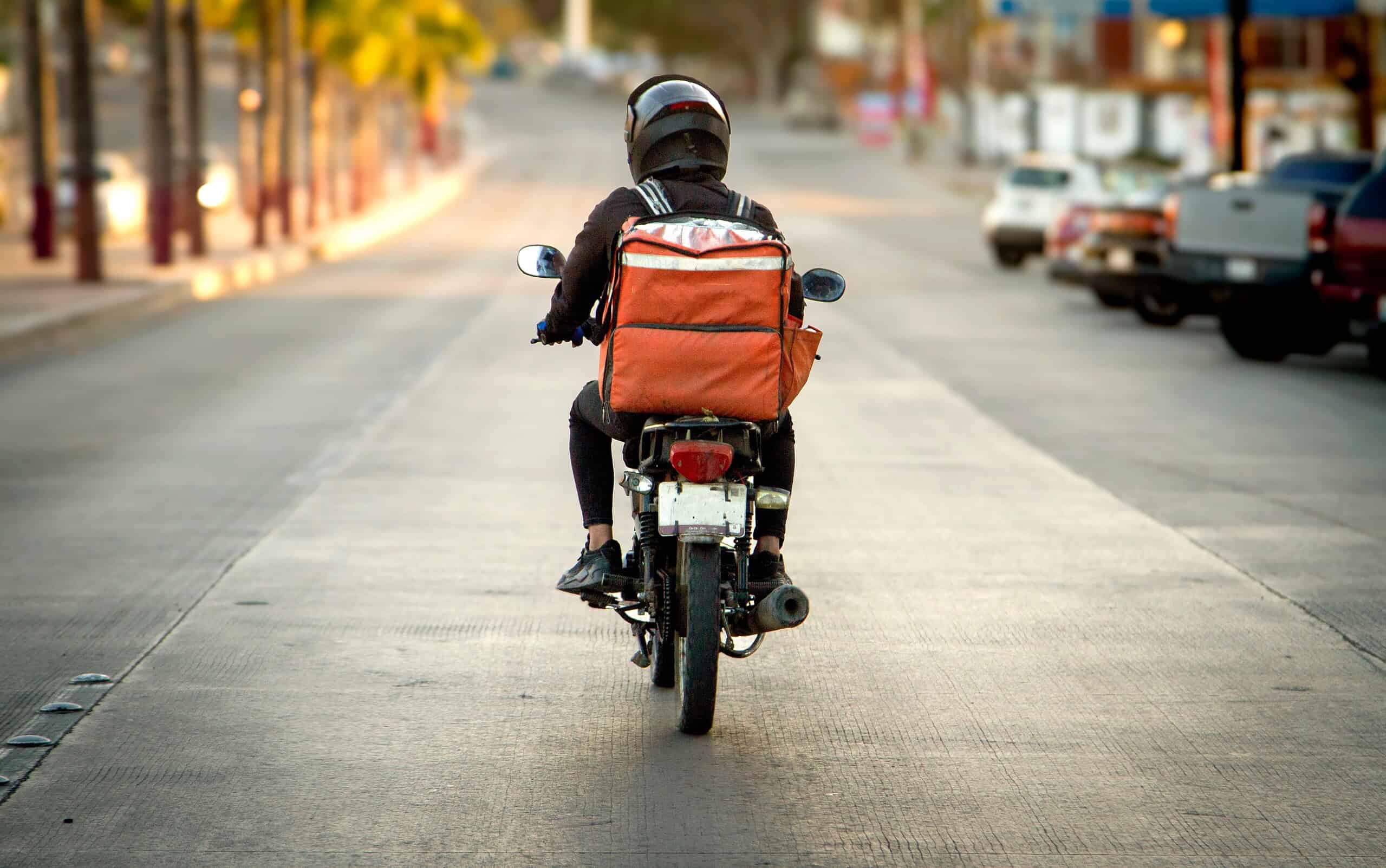 Motorcycle rider with backpack on city street during daytime.